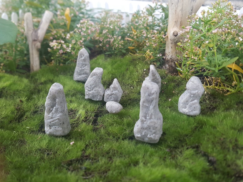 Może przedstawiać: Miniaturowy ogr&oacute;d kamienny z siedmioma szarymi kamiennymi figurami ułożonymi w k&oacute;łko na ł&oacute;żku z zielonego mchu.