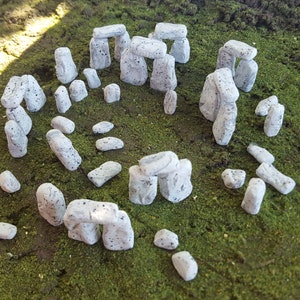 May include: A miniature model of Stonehenge made of white stone with a speckled texture. The model is set on a bed of green moss.