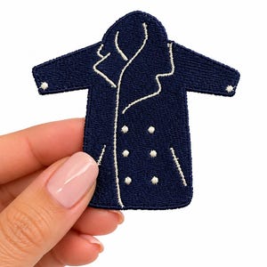 May include: A dark navy blue embroidered patch shaped like a double-breasted coat. The patch features white stitched detailing outlining the lapels, the front opening, two pockets, and six small circular buttons arranged in two vertical rows.