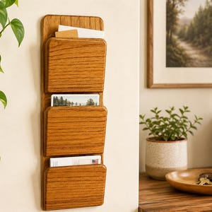 Puede incluir: Un organizador de pared de madera con tres bolsillos. El organizador es de madera marrón claro y contiene varias tarjetas y papeles. El diseño es simple y funcional, adecuado para el hogar o la oficina.
