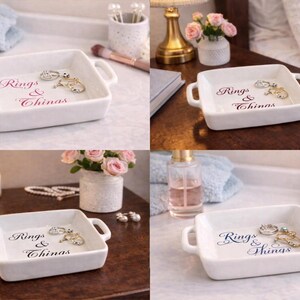 May include: A white square ceramic dish with handles, holding rings and other jewelry. The dish has the words "Rings & Things" in a script font. The jewelry includes silver and gold rings.