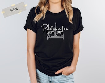 Pode incluir: Camiseta preta com o texto "Pilates is for every body" e uma silhueta de uma pessoa fazendo pilates em um reformer.