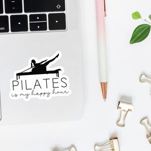 May include: A white sticker with a black silhouette of a person doing pilates on a reformer. The text "PILATES is my happy hour" is written below the silhouette.