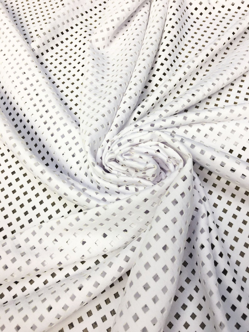 May include: White fabric with a square-shaped cut-out pattern. The fabric is folded and draped.