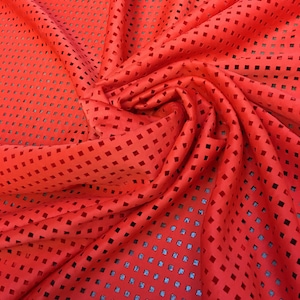 May include: Red fabric with a square-shaped cut-out pattern. The fabric is folded and draped.