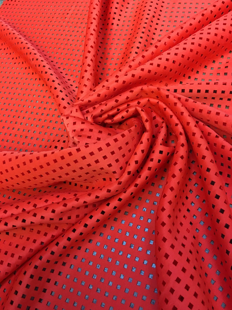 May include: Red fabric with a square-shaped cut-out pattern. The fabric is folded and draped.