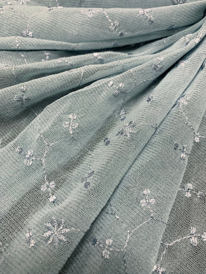 May include: Pale blue tulle fabric with a delicate white floral embroidery pattern.