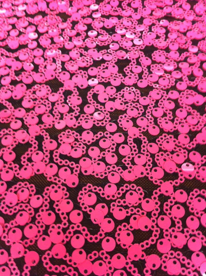 May include: Pink sequins on a black mesh fabric. The sequins are arranged in a swirling pattern.