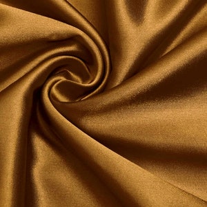 May include: A close-up of a smooth, golden brown satin fabric. The fabric is draped and folded, creating soft, flowing lines.