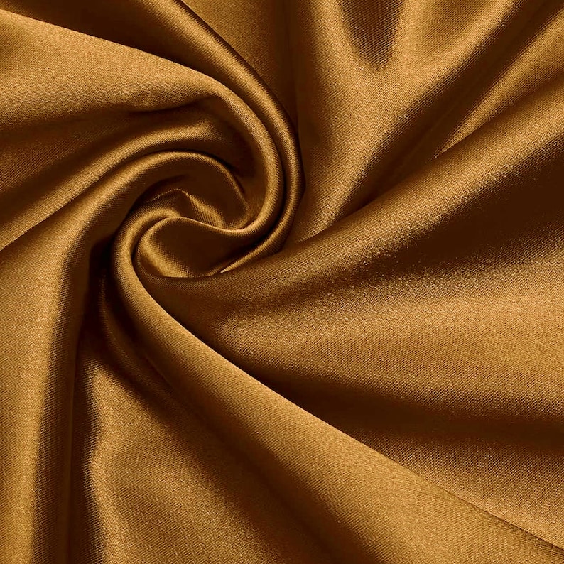 May include: A close-up of a smooth, golden brown satin fabric. The fabric is draped and folded, creating soft, flowing lines.