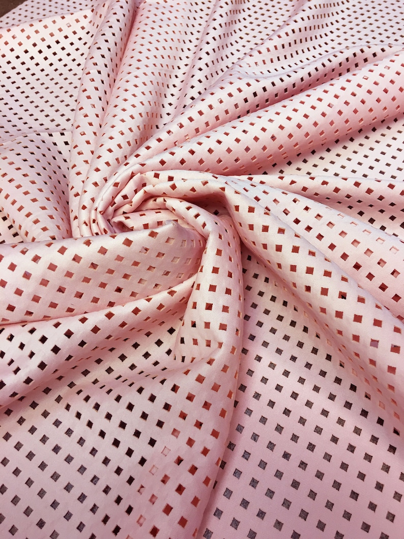 May include: Pink fabric with a square pattern cut-out design. The fabric is soft and has a delicate texture.