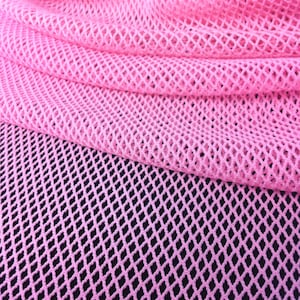 May include: Close-up of a pink mesh fabric with a diamond pattern. The fabric is draped, creating folds and shadows. The background is black, providing contrast to the bright pink material. The texture of the mesh is clearly visible.