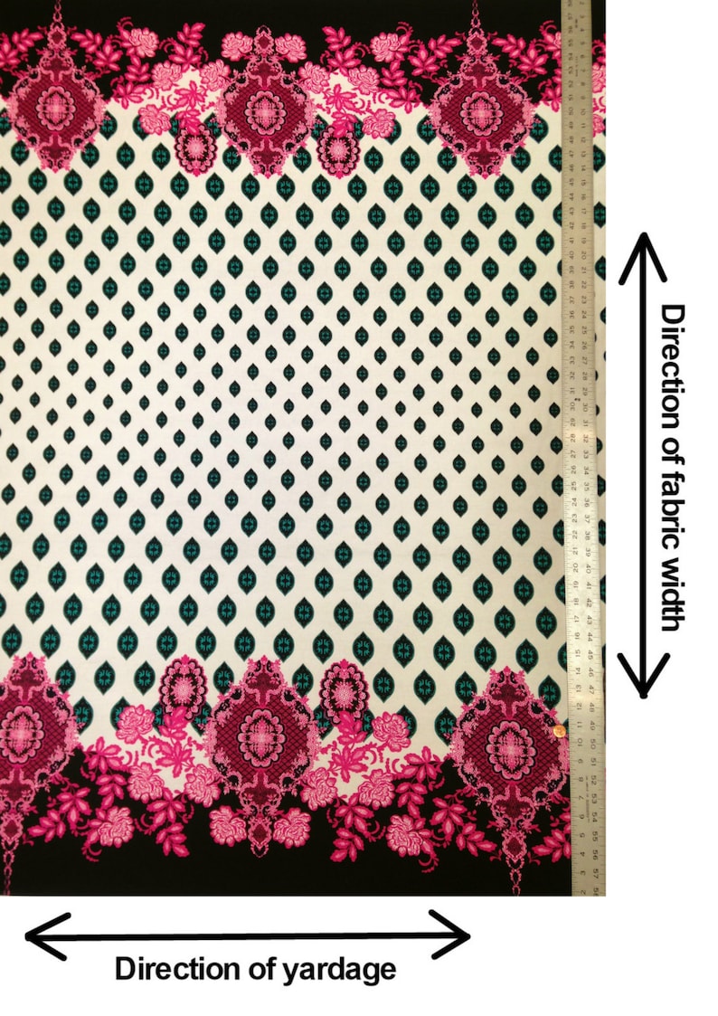 May include: A white fabric with a black background and a repeating pattern of teal and black diamonds. The fabric has a pink and black floral border with intricate designs. The fabric is 58 inches wide.