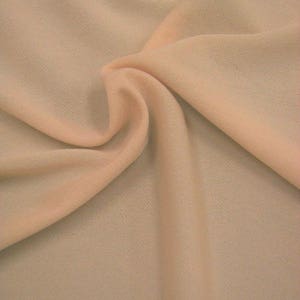 May include: A close-up of a pale peach coloured fabric with a slightly textured surface. The fabric is folded and draped, showing its soft and flowing nature.