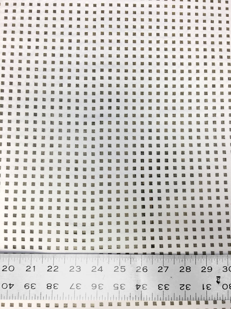 May include: A white sheet of paper with a grid pattern of small, evenly spaced squares. A metal ruler is placed at the bottom of the sheet, with the numbers 20 through 30 visible.