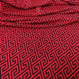 May include: Red fabric with a black geometric pattern. The pattern is a repeating design of interlocking squares and rectangles.