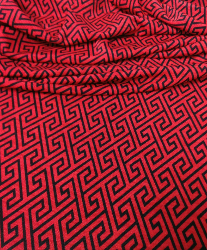 May include: Red fabric with a black geometric pattern. The pattern is a repeating design of interlocking squares and rectangles.