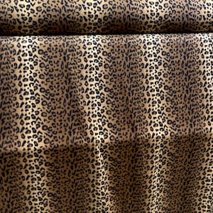 Könnte beinhalten: Nahaufnahme eines braunen und goldenen Stoffes mit Leopardenmuster. Der Stoff ist aufgerollt und das Muster ist auf beiden Seiten der Rolle sichtbar.