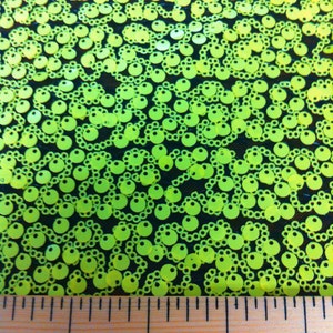 May include: Close-up of neon green sequins on a black mesh fabric. A ruler is placed at the bottom of the image, showing measurements in inches.