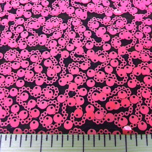 May include: Pink sequins on a black mesh fabric. A ruler is placed at the bottom of the image with the numbers 10, 11, and 12 visible.