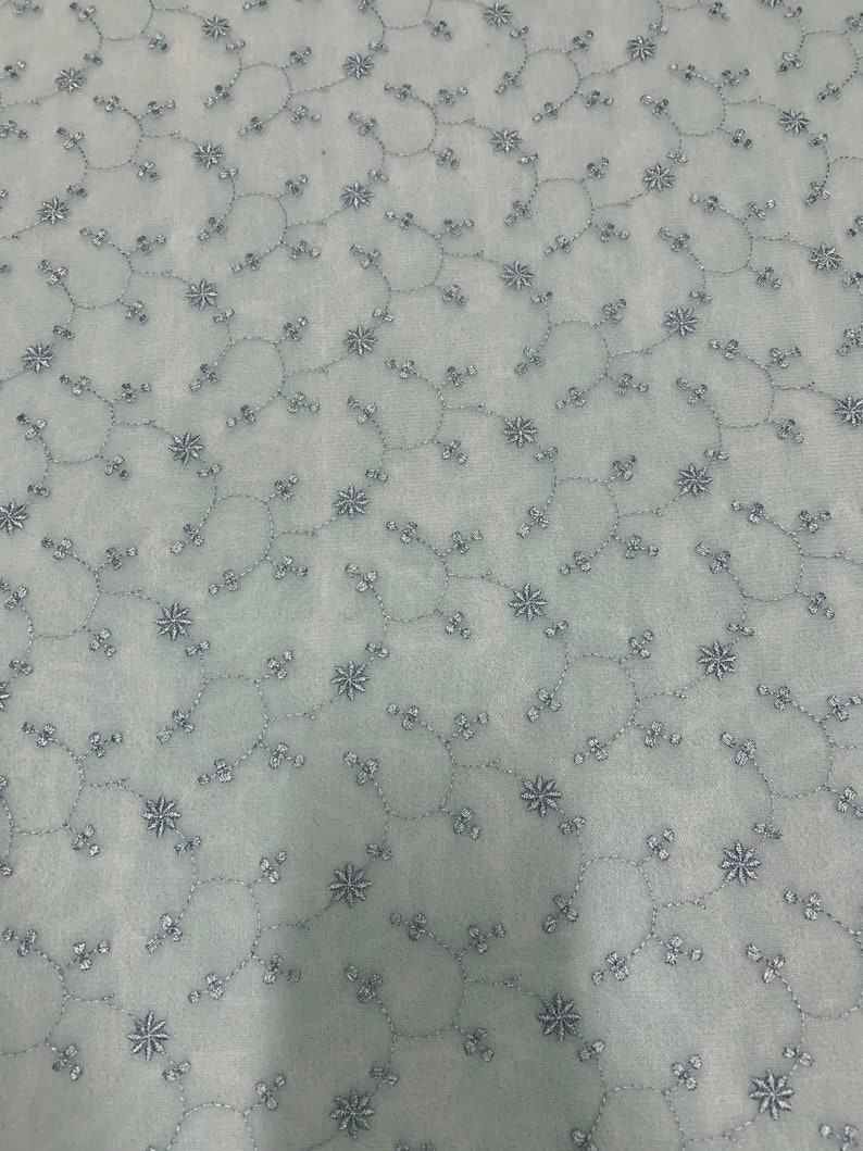 May include: A light blue fabric with a delicate pattern of embroidered silver flowers and vines.