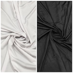 May include: Two fabric swatches, one white and one black, are shown in a crumpled, folded, and draped style. The fabric is smooth and has a slight sheen.