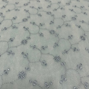 May include: A light blue sheer fabric with a delicate floral embroidery pattern in silver thread.