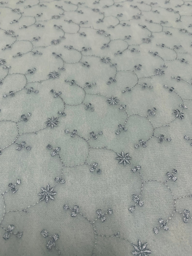 May include: A light blue sheer fabric with a delicate floral embroidery pattern in silver thread.