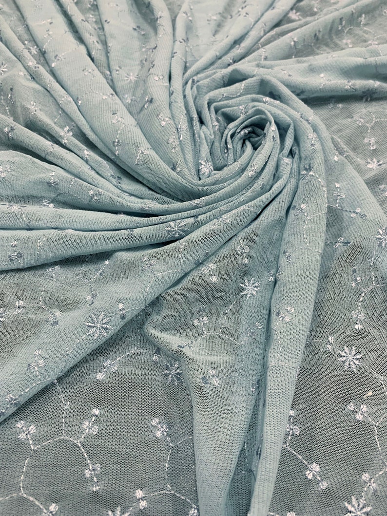 May include: Light blue sheer fabric with a delicate floral embroidery pattern. The fabric is gathered and twisted, creating a soft, flowing texture.