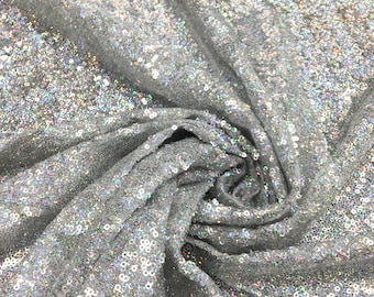 May include: Silver fabric covered in small, round sequins. The fabric is draped, creating folds and shadows that highlight the texture and sparkle of the sequins. The text "Silver SQN-9-R" is visible.
