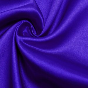 May include: A close-up of a smooth, silky fabric in a deep, rich purple color. The fabric is draped and folded, creating soft, flowing lines and curves.