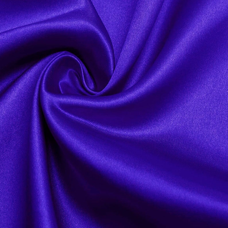 May include: A close-up of a smooth, silky fabric in a deep, rich purple color. The fabric is draped and folded, creating soft, flowing lines and curves.