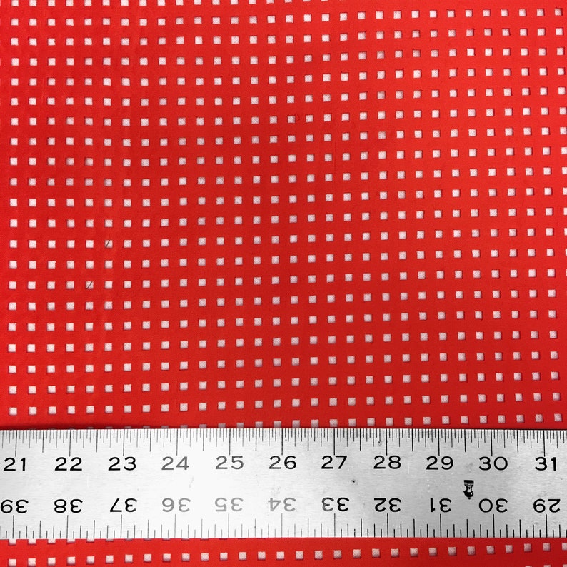 May include: Red fabric with a white grid pattern. A ruler is placed at the bottom of the image with the numbers 21 to 31 visible.