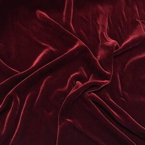 May include: A close-up of a deep red velvet fabric with soft, flowing folds. The fabric has a luxurious and elegant appearance.