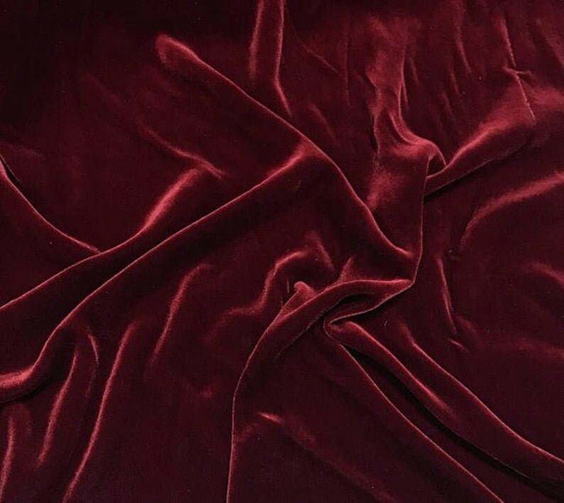 May include: A close-up of a deep red velvet fabric with soft, flowing folds. The fabric has a luxurious and elegant appearance.