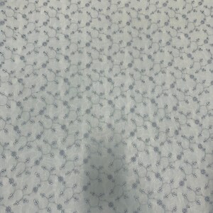 May include: A white fabric with a delicate embroidered pattern of small flowers and vines. The fabric has a subtle sheen and a soft texture.