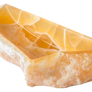 May include: A large, natural, yellow onyx bowl with a rough, irregular exterior and a smooth, polished interior. The bowl is made of natural stone and has a unique, organic shape.