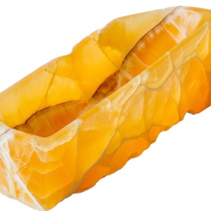 May include: A yellow onyx dish with a natural, rough-hewn design. The dish is made of polished stone and has a smooth, glossy finish.