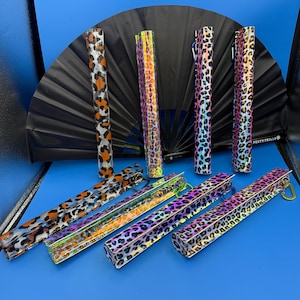May include: A set of eight iridescent leopard print fan cases with a black fan in the background. The cases are made of a clear plastic material with a leopard print design. The cases have a silver zipper and a silver ring.