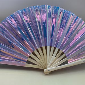 May include: A iridescent blue and purple hand fan with a wooden handle. The fan is closed and has the text "Festy Frills" printed on the handle.