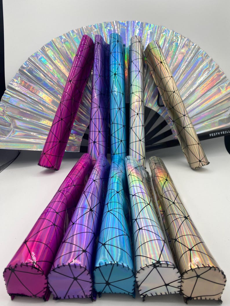 Puede incluir: Ocho portacepillos de maquillaje hologr&aacute;ficos iridiscentes con un patr&oacute;n geom&eacute;trico y costuras negras. Los portacepillos est&aacute;n dispuestos en una fila, con los extremos de los portacepillos mirando hacia el espectador. Los portacepillos son de varios colores, incluyendo rosa, morado, azul y dorado.