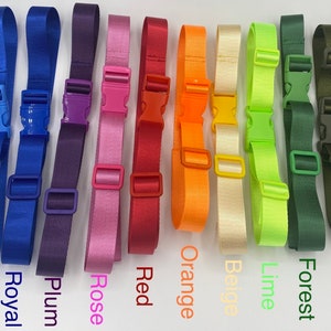 Może przedstawiać: Asortyment 10 kolorów regulowanych pasków z plastikowymi klamrami. Kolory obejmują biały, niebieski, granatowy, śliwkowy, różowy, czerwony, pomarańczowy, beżowy, limonkowy, zielony leśny, oliwkowy i czarny.