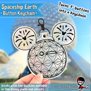 May include: A silver holographic keychain featuring a geodesic sphere design with two circular ears, each embroidered with black firework patterns. The keychain includes a black metal lobster clasp and is designed to hold 7.62 cm buttons.