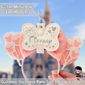 May include: A pink Minnie Mouse ear holder with a white bow embroidered with the name "Tiffany" in silver. The holder has a silver clasp and is decorated with sequins and Mickey Mouse balloon designs. Text on the image reads "Custom Minnie Bow EAR HOLDER".