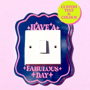 Peut inclure: Un cache-interrupteur avec un fond bleu et une bordure rose. Le cache porte le texte "Have a Fabulous Day" en lettres roses avec des étoiles de chaque côté du texte.