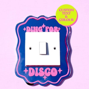 Puede incluir: Una cubierta de interruptor de luz azul y rosa con el texto "DING FOR DISCO" en letras rosas. La cubierta del interruptor está decorada con estrellas. Un círculo amarillo con el texto "CUSTOM TEXT & COLOUR" está en la esquina superior derecha de la imagen.