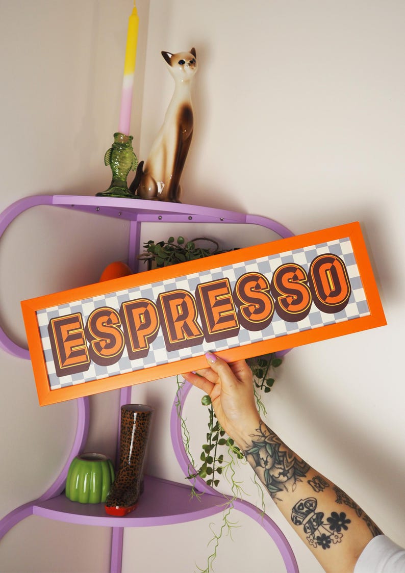 May include: An orange framed sign with the word "ESPRESSO" in brown and orange retro font. The background is a checkered pattern of gray and white. The sign is being held up in front of a purple shelf with decorative items.