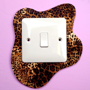 Könnte beinhalten: Ein weißer Lichtschalter mit einer Leopardenmuster-Umrandung. Der Schalter befindet sich an einer rosa Wand.