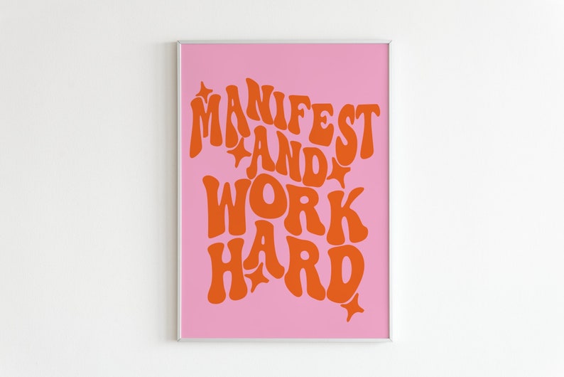 May include: A pink poster with the text "MANIFEST AND WORK HARD" in orange, retro-style lettering. The text is surrounded by small white stars.