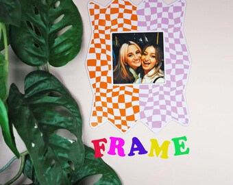 May include: A colorful magnet frame with a photo of two smiling people. The frame has a checkered pattern in orange and purple. The word "MAGNET" is above the frame, and "FRAME" is below, in bright, multi-colored letters.